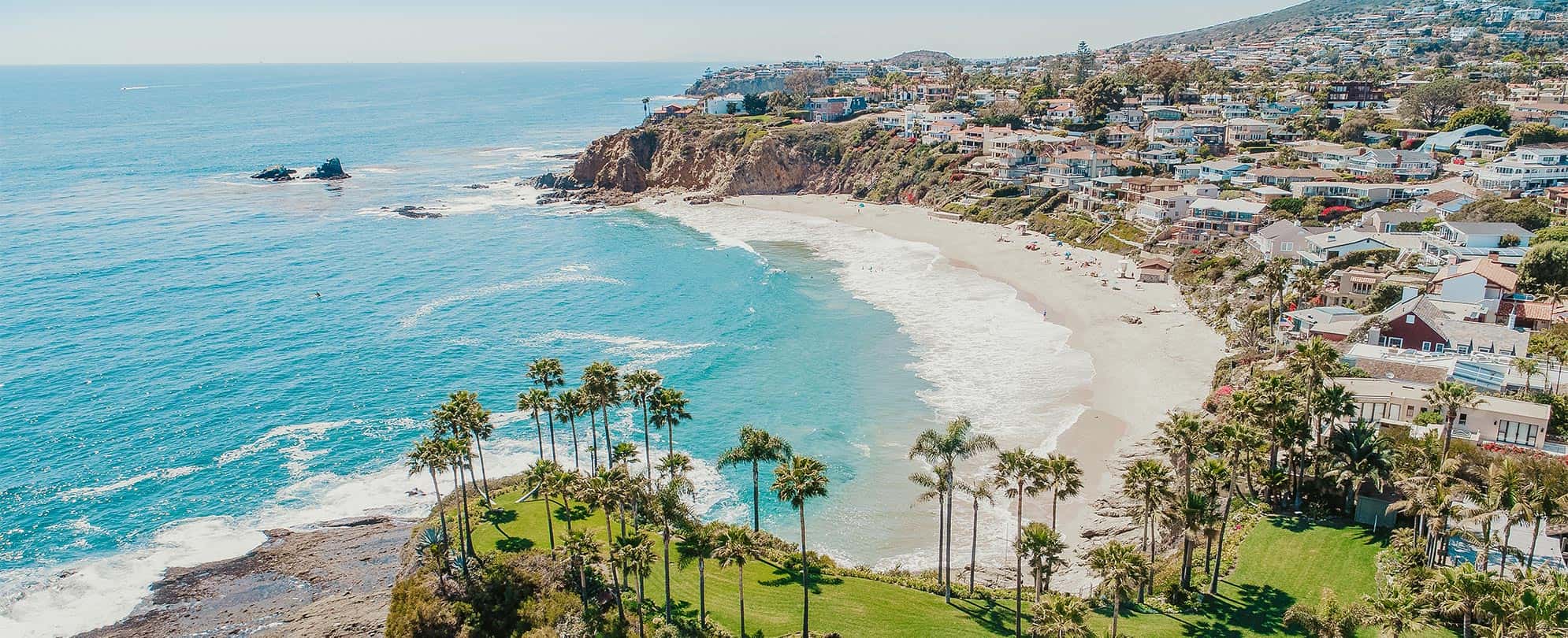 The ocean, sand, and surrounding houses and palm trees at Laguna Beach in California.
