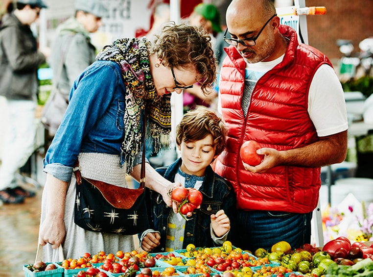 A man, woman, and child hold tomatoes while they shop for vegetables at The Municipal Market in Atlanta, Georgia.