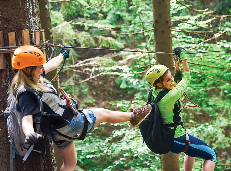 Two female caucasian friends zip-lining in the woods. 