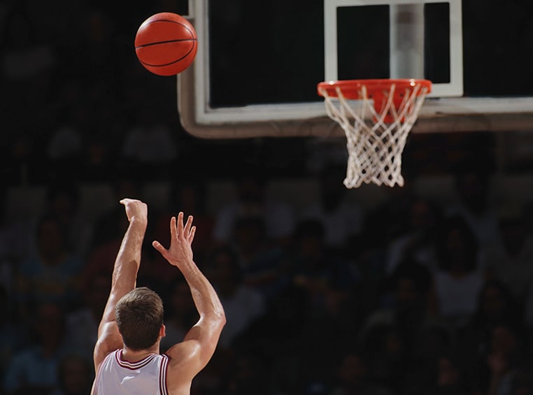 A caucasian male is shooting a basketball at the hoop.