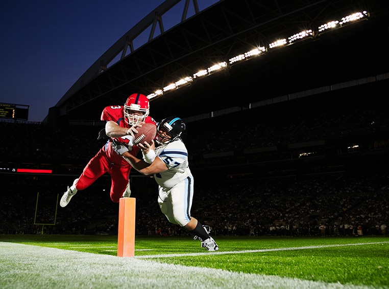 A football player is diving towards the endzone with a football.