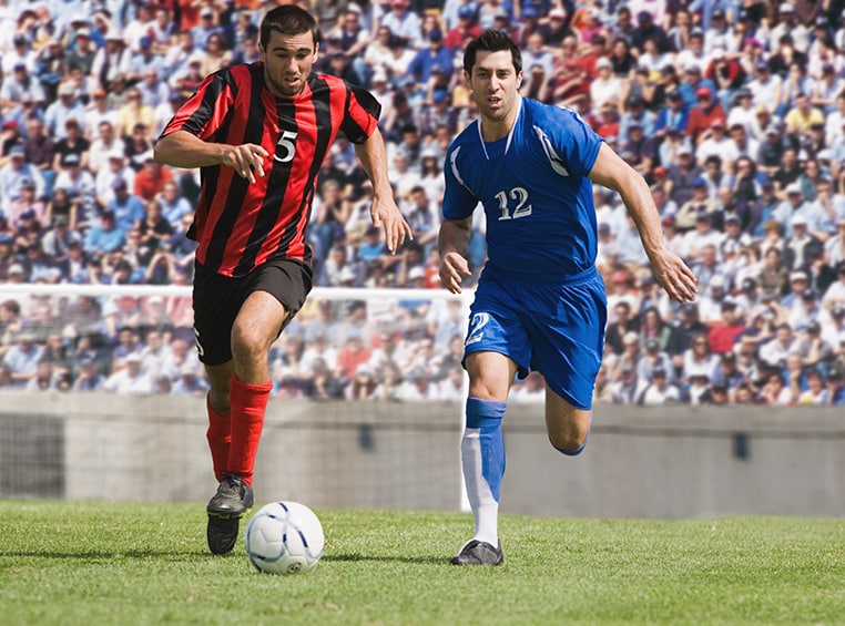 Two male soccer players race towards a soccer ball.