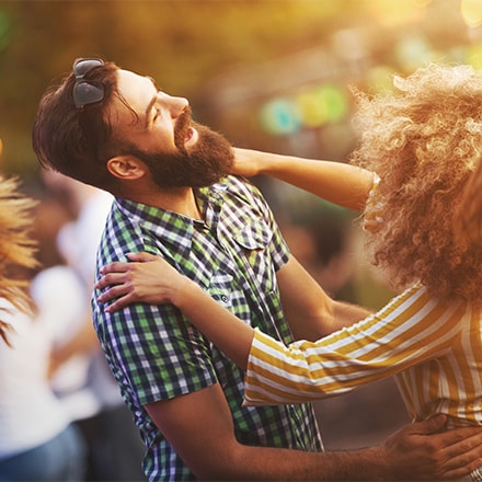 A caucasian man with a beard is dancing with an african american female with curly golden hair.