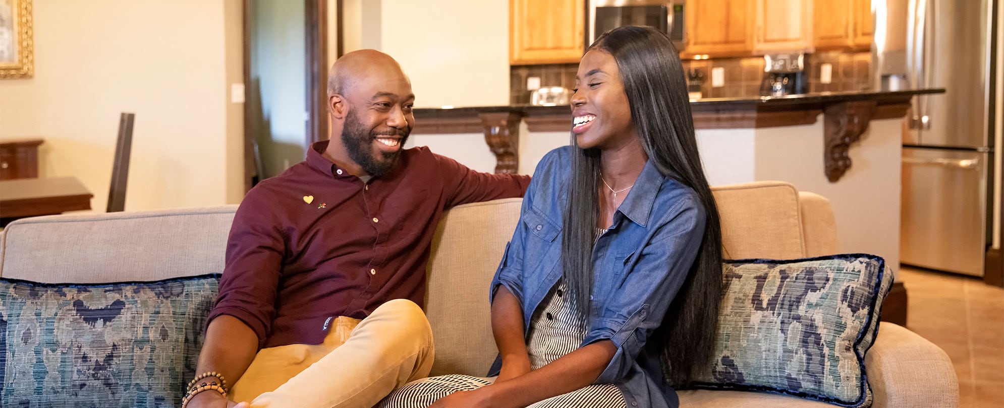 An african american couple laugh while sitting on a sofa in a hotel room.
