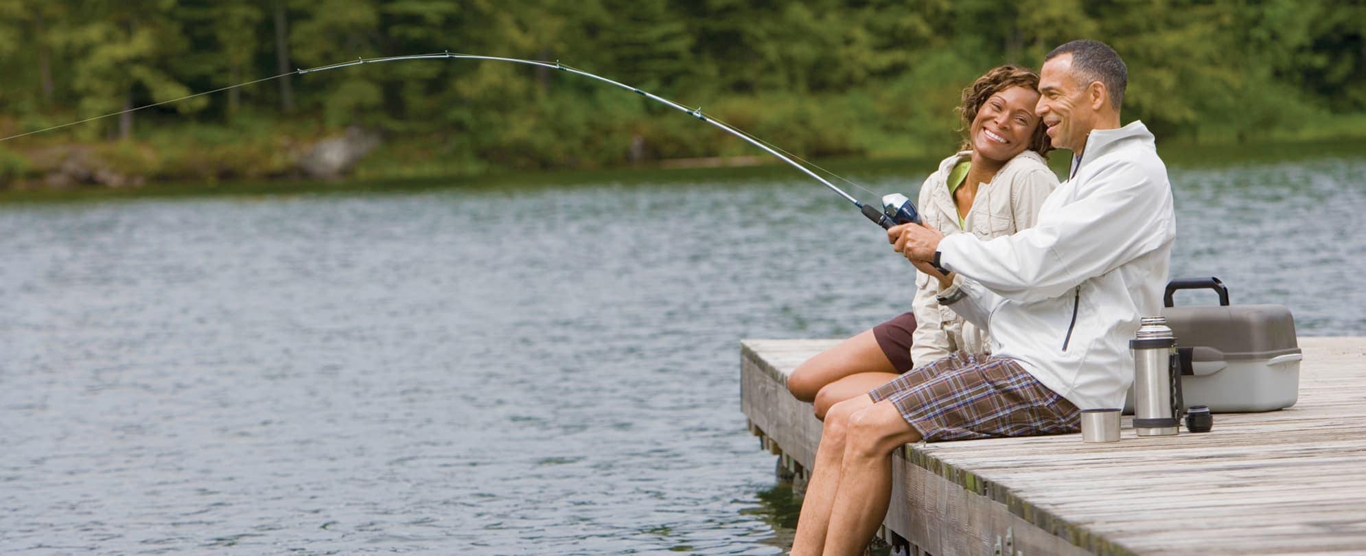 A man and woman sit smiling on a dock, casting a fishing line into Table Rock Lake.