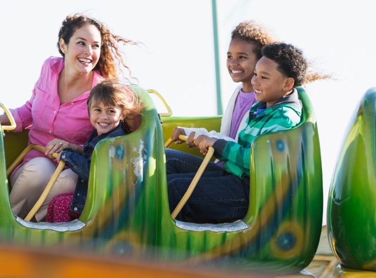 Kids and adults riding a children's rollercoaster at one of the Orlando theme parks.