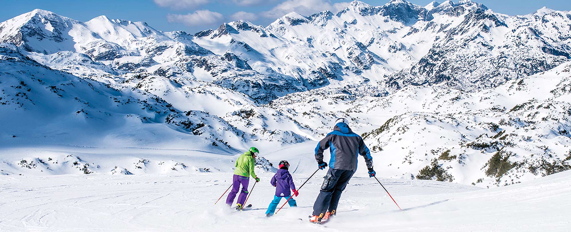 A dad and two kids skiing in Whistler, Colorado, with the snowy mountains in the background.