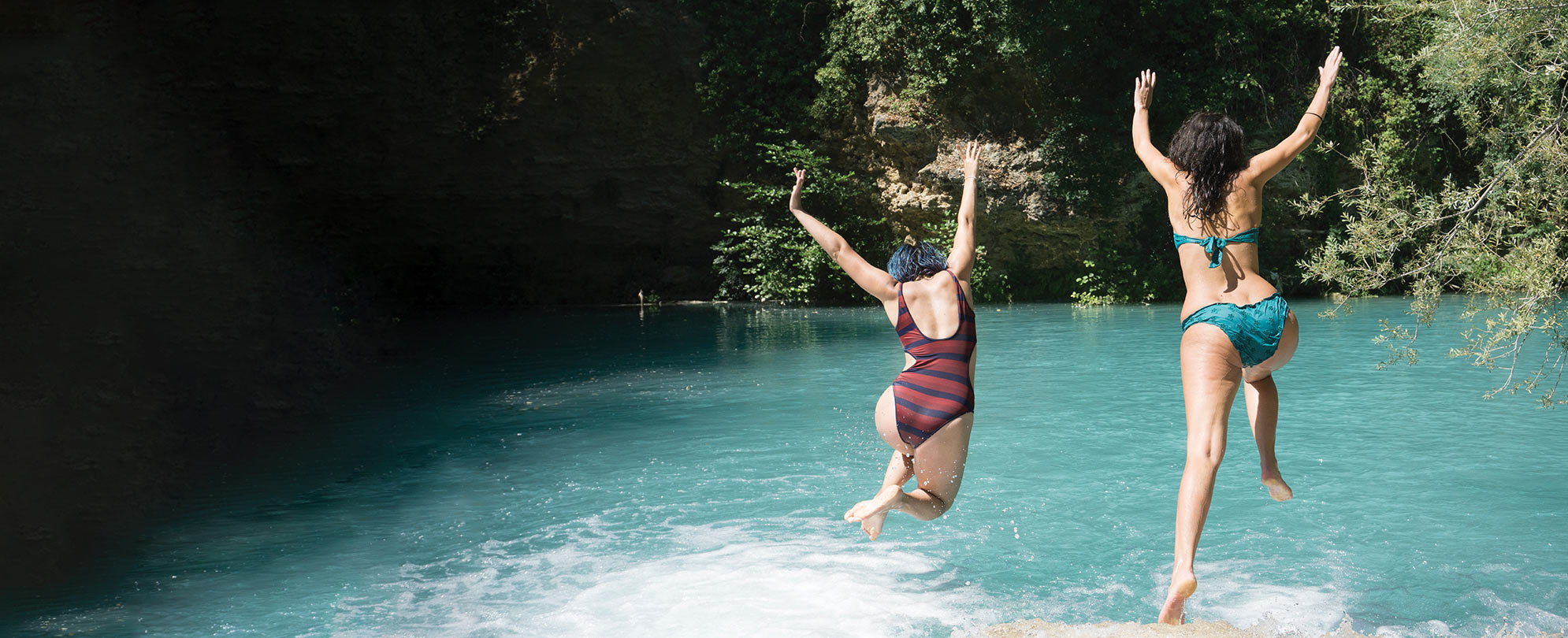 Two woman with their arms up jump into a lake on a trip with Club Wyndham Travel Packages.