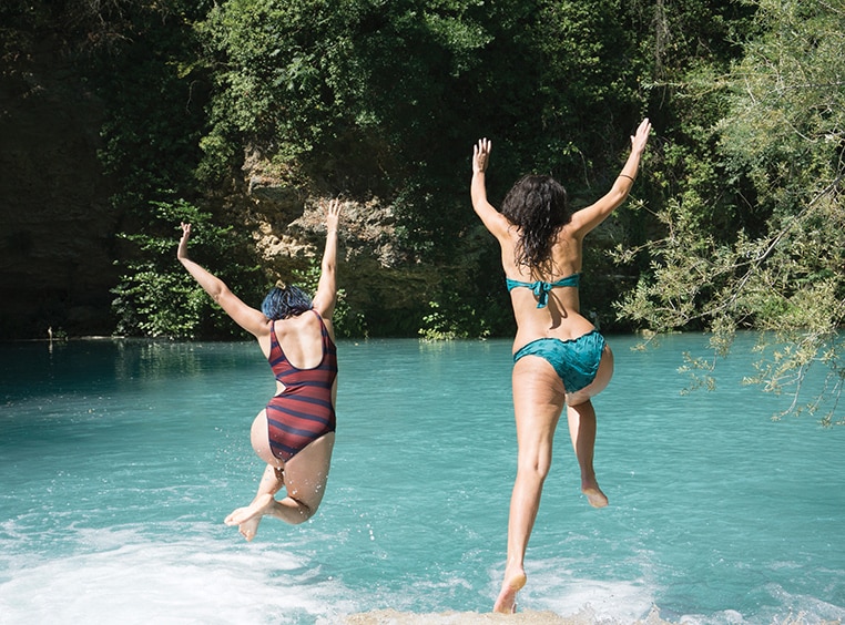 Two woman with their arms up jump into a lake on a trip with Club Wyndham Travel Packages.