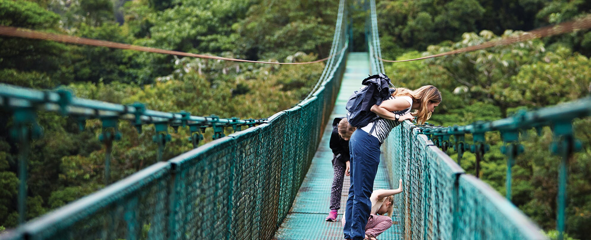 Woman and two kids looking off the side of a suspended bridge in the jungle during a tour of Costa Rica.
