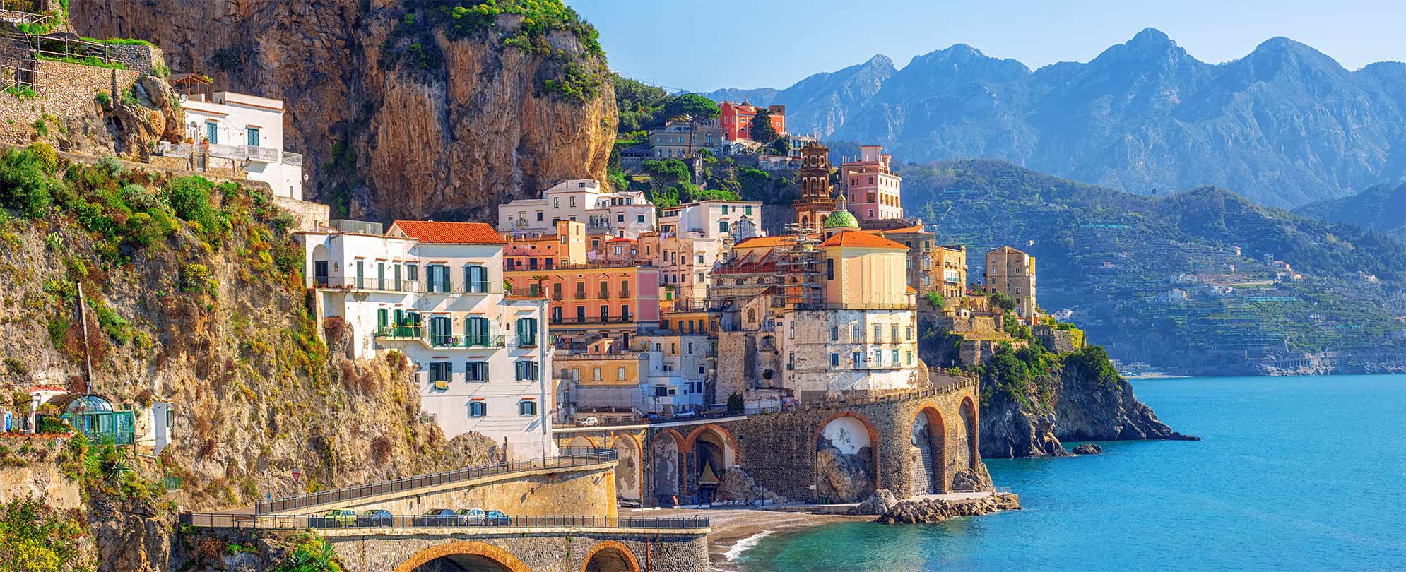 The Amalfi Coast in Southern Italy with buildings in a mountainside, ocean, and a winding coastal road.