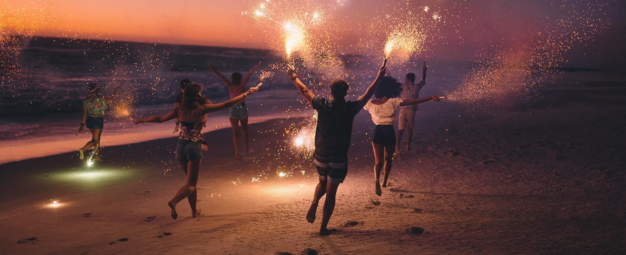 Six friends running on the beach with sparklers in their hand after sundown. 