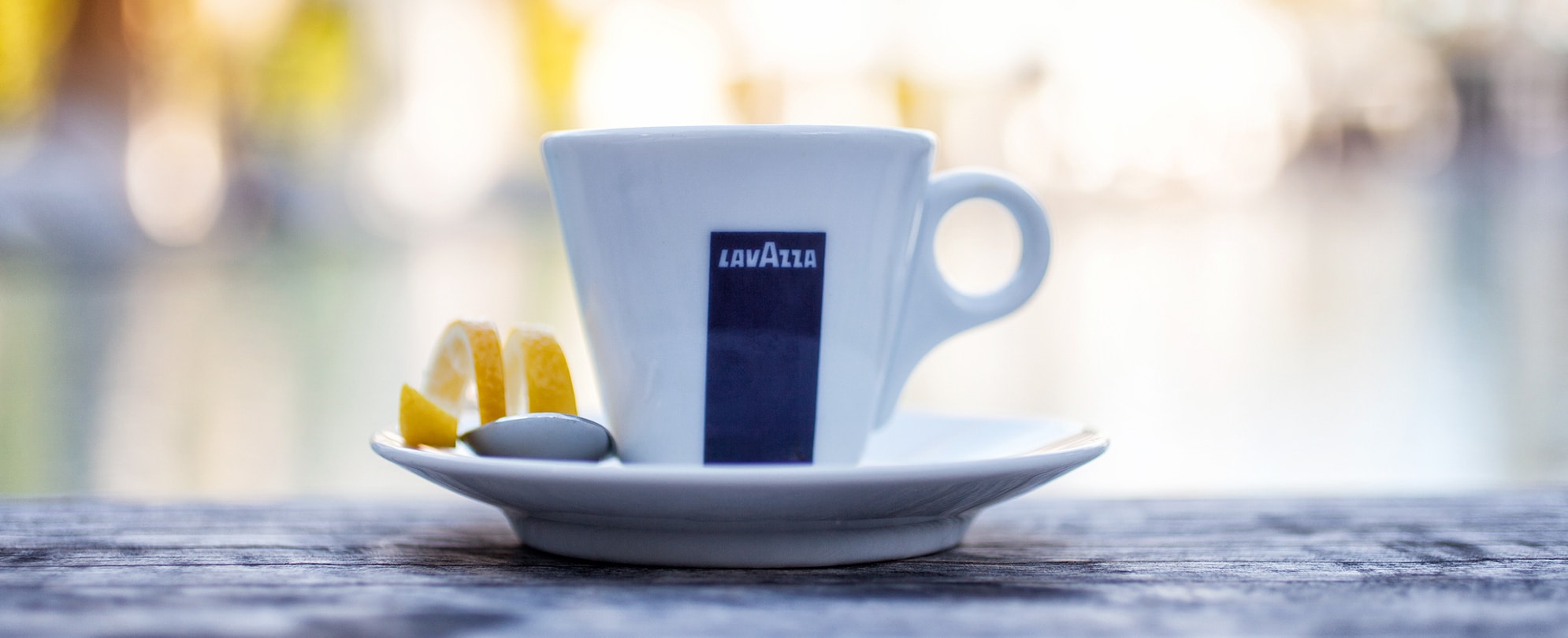 A Lavazza espresso cup and saucer with a lemon peel on the side. 
