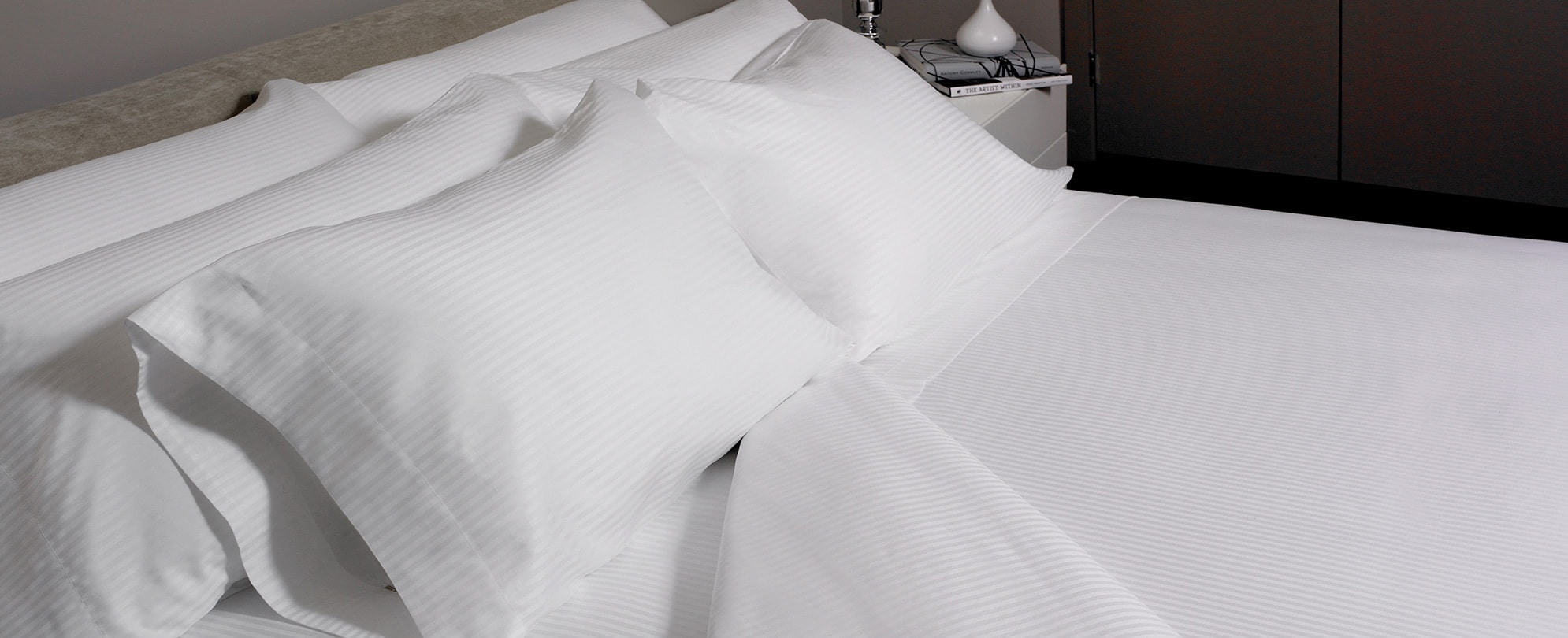A made queen bed with six fluffy pillows, and the right corner of the white sheets folded down. 