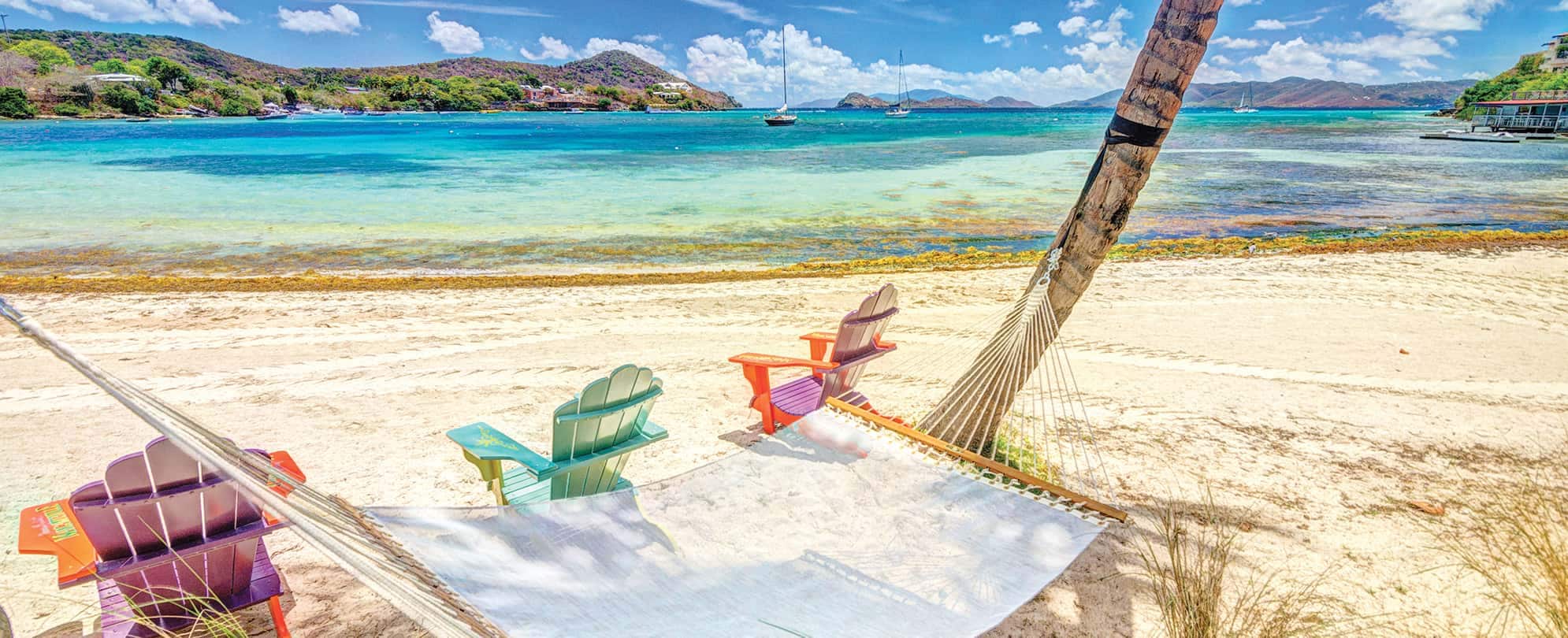 Three beach chairs and a hammock on a tropical beach near clear blue waters