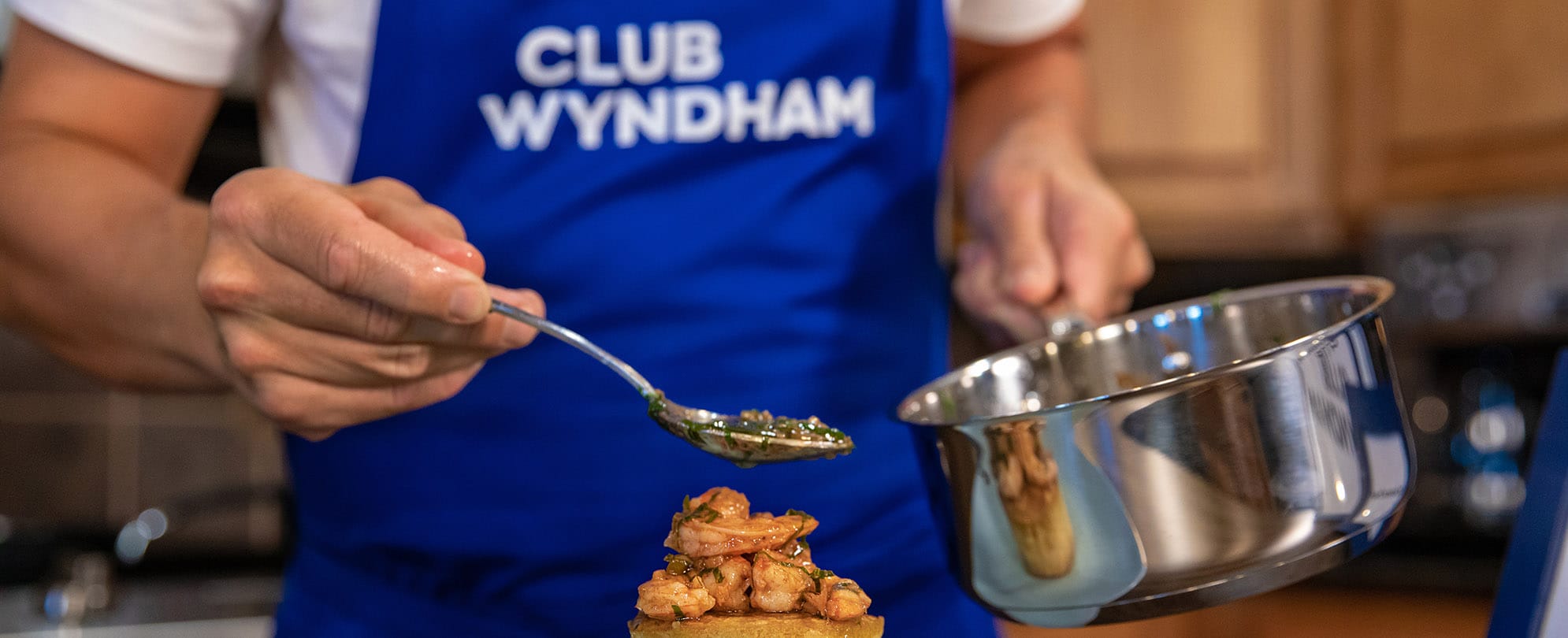 A chef in a Club Wyndham apron prepares a shrimp meal.