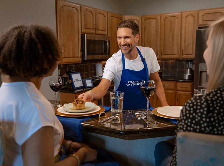 2 women get served a meal by a private chef in their Club Wyndham resort suite.