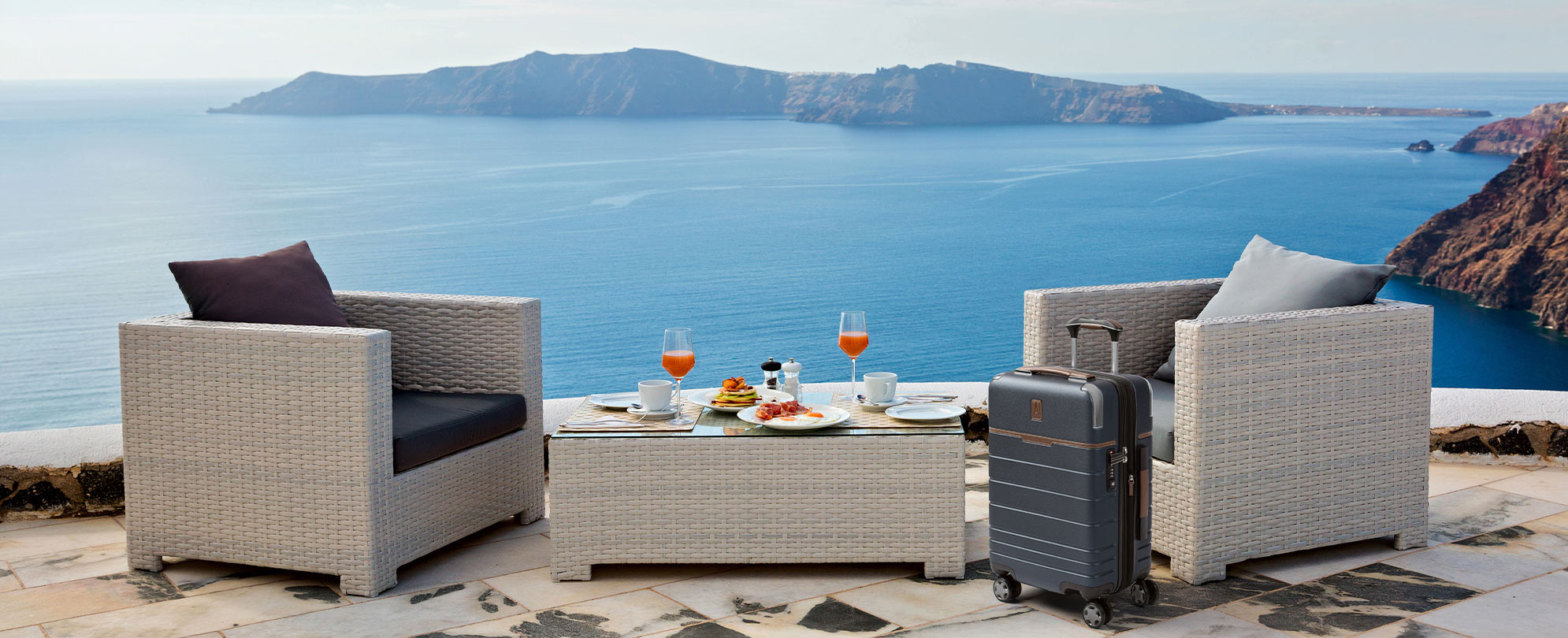 A TravelPro suitcase in front of two outdoor chairs with an ocean view and a coffee table with food.