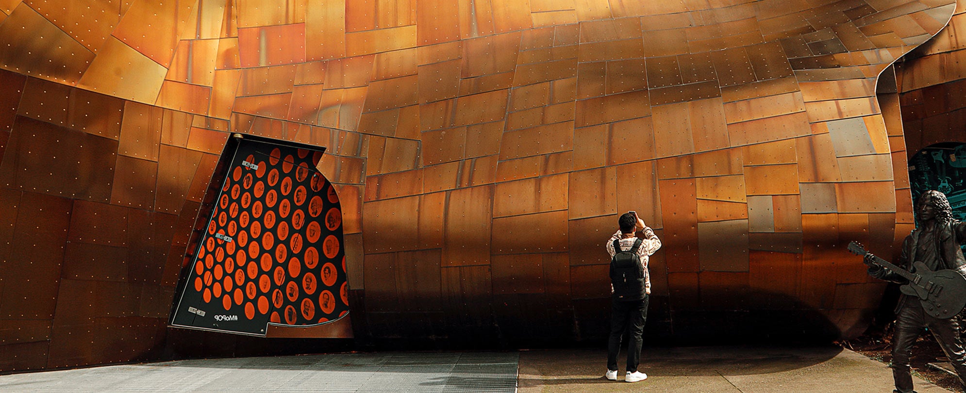 A man with a backpack holds up his phone to take a photo of the Museum of Pop Culture in Seattle