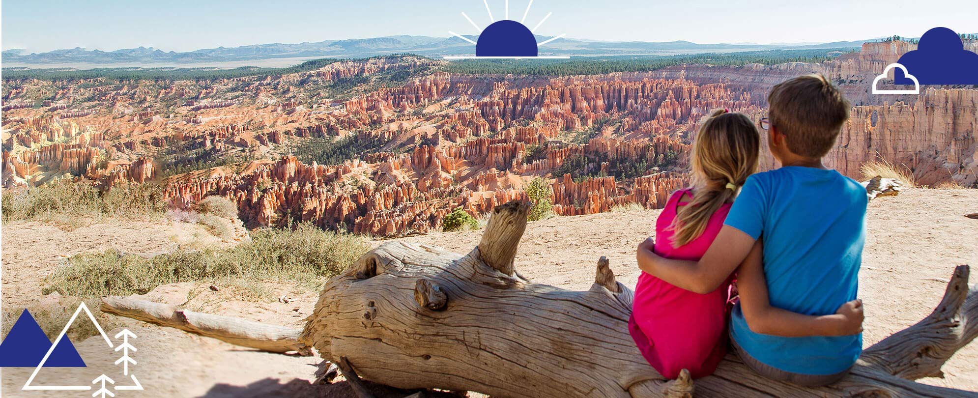 A young boy and girl and sit with their arms around eachother as they look out over a large desert canyon