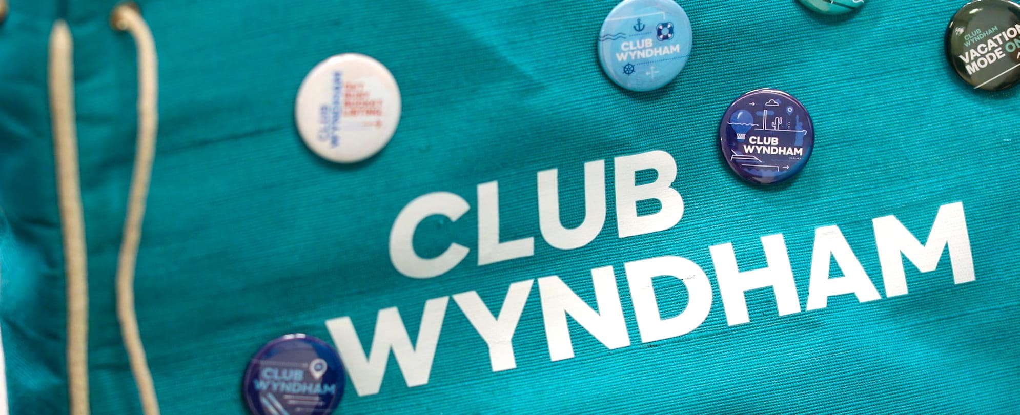 A teal Club Wyndham bag with six Pinspiration pins pinned on the bag