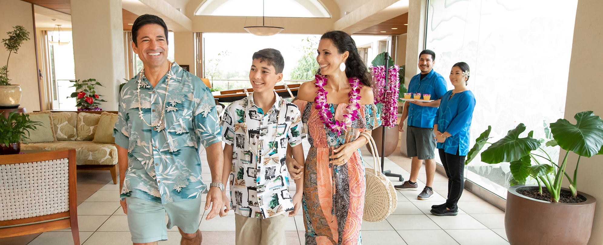 A mom, dad, and son walk through a Club Wyndham resort lobby smiling and wearing leis on their summer vacation.