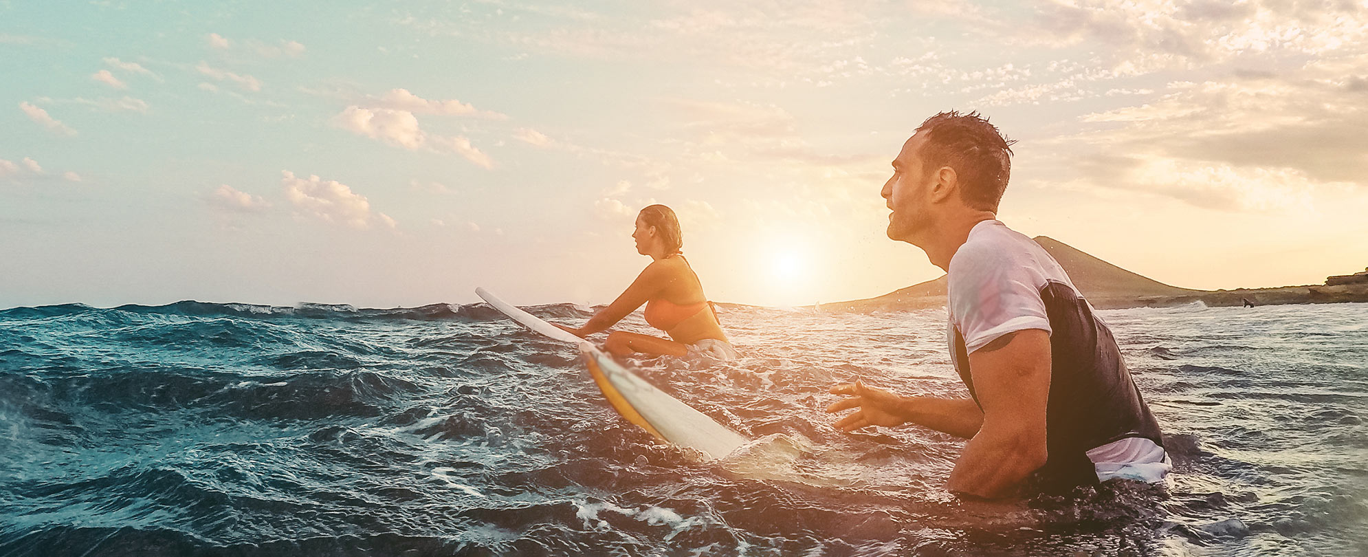 A man and woman out in the ocean with their surfboards waiting for the next wave. 
