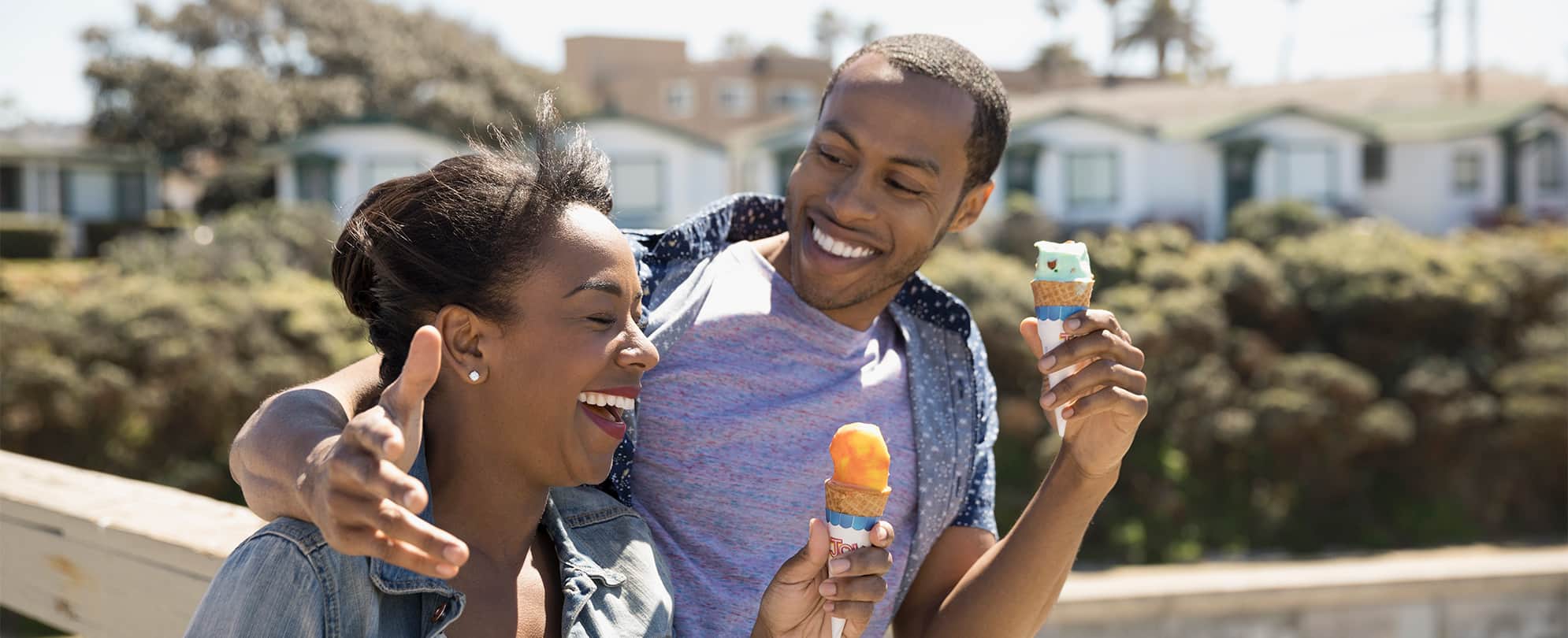 A man leisurely walks with his arm around a woman’s shoulder, they are both smiling and holding ice cream cones.