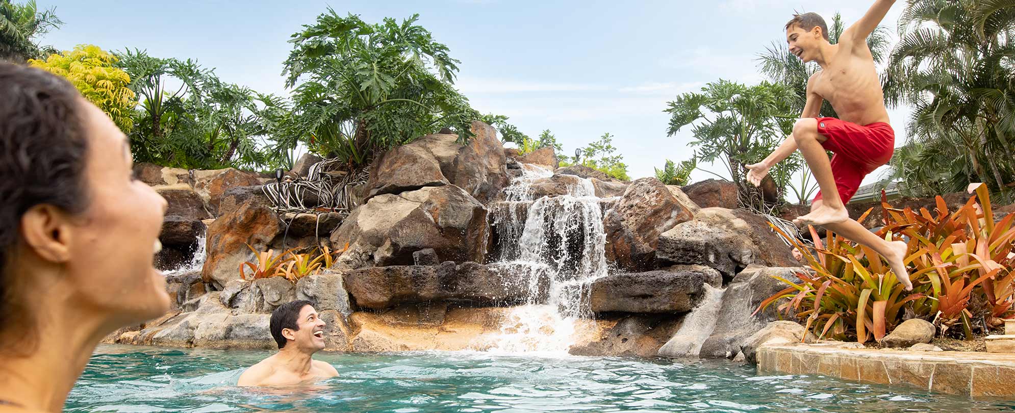 A boy jumps into a tropical Club Wyndham resort pool while his parents smile