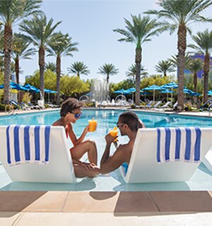 A couple, sitting next to each other in lounge chairs while drinking a cocktail poolside at a Club Wyndham resort.