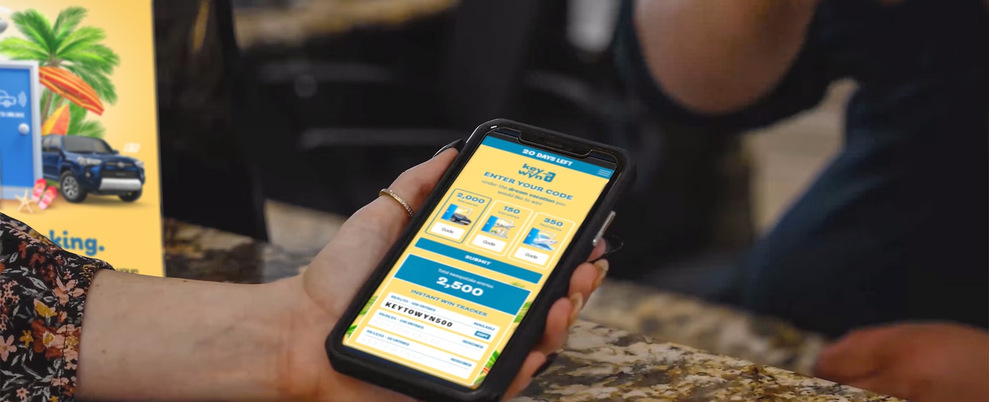 A woman's hand holds a smartphone with the yellow and blue Key To Wyn landing page loaded onto the screen.