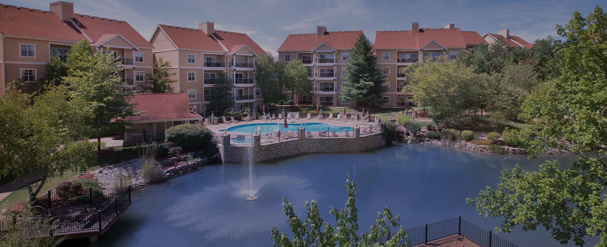 The exterior of Club Wyndham Branson at the Meadows overlooking an outdoor pool and a small lake with a fountain.