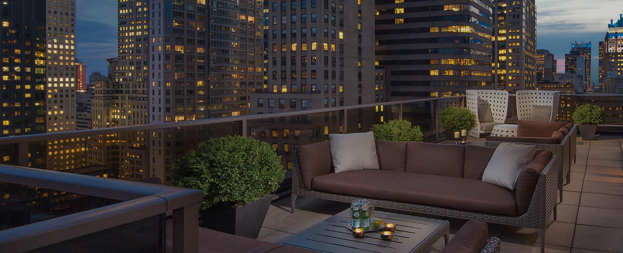 The rooftop deck with couches and chairs at Club Wyndham Midtown 45; New York City skyscrapers lit up in the background. 