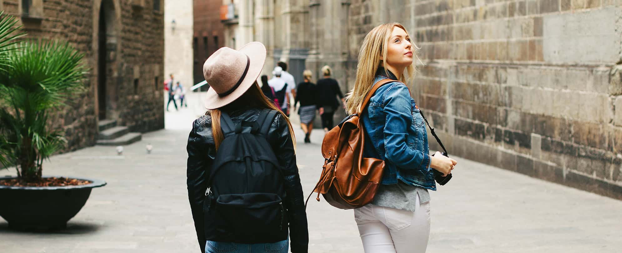 Two young women wearing backpacks walk through the city of Barcelona, Spain.