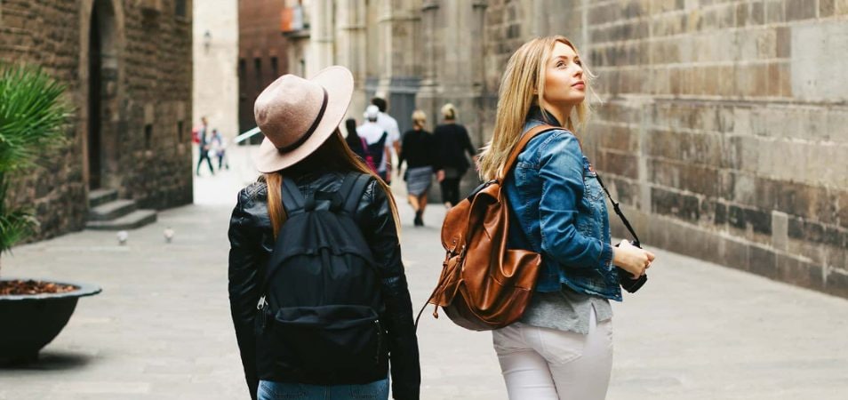 Two young women wearing backpacks walk through the city of Barcelona, Spain.