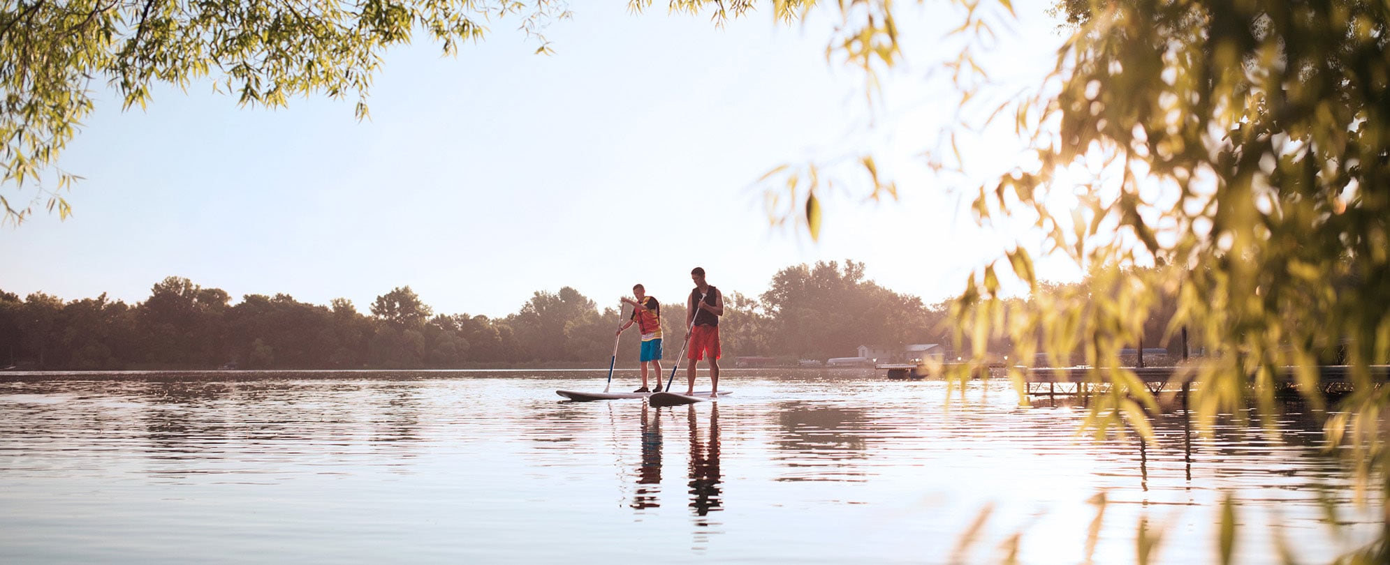 A father and son paddle board around a lake in the Midwest while on vacation