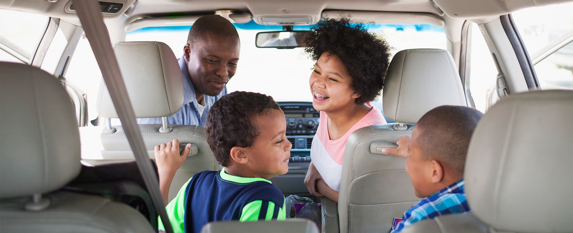 Dad and mom in the front seat of a car, turn around to look at two young boys.