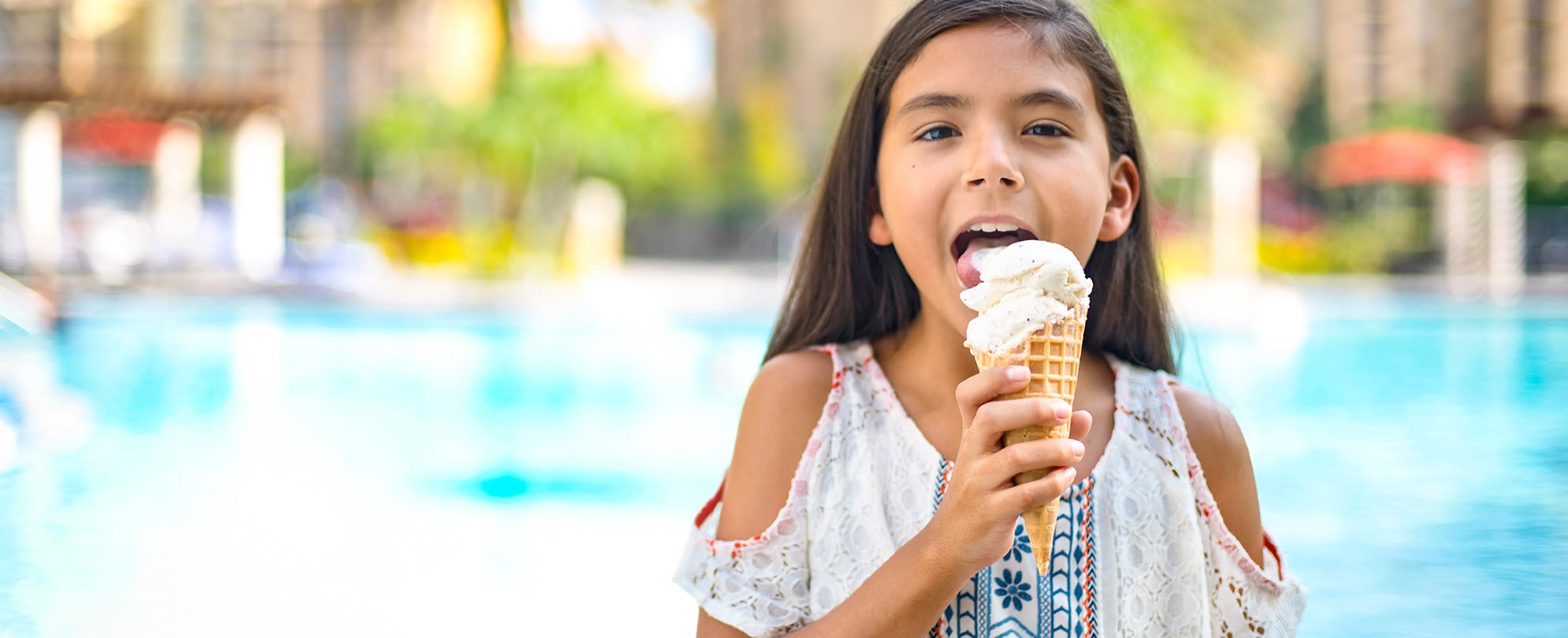 A young girl licks a vanilla ice cream waffle cone by the pool at a Club Wyndham resort