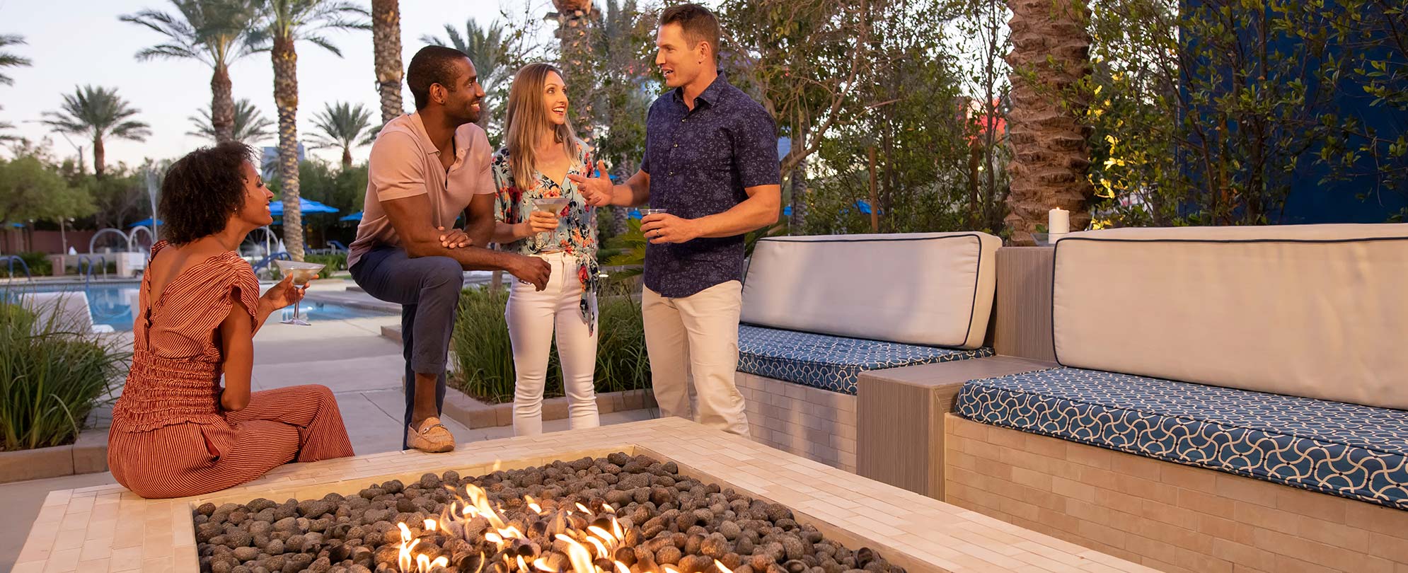 Four friends talk and drink around the firepit at Club Wyndham Desert Blue in Las Vegas on a summer vacation.