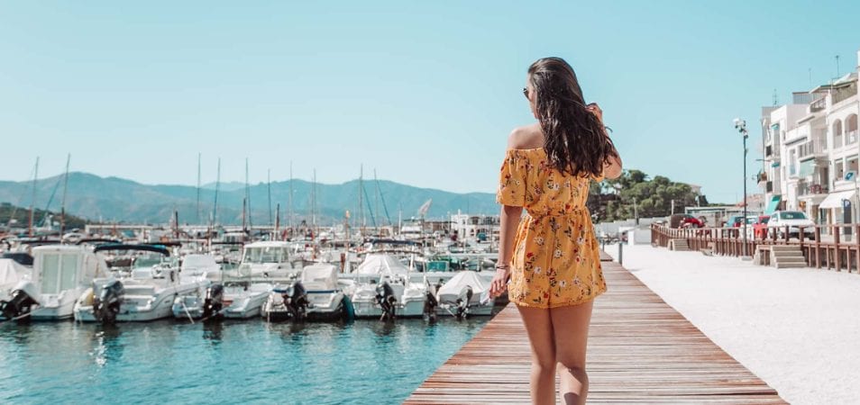 A woman in a yellow romper walks along a marina dock on a summer day