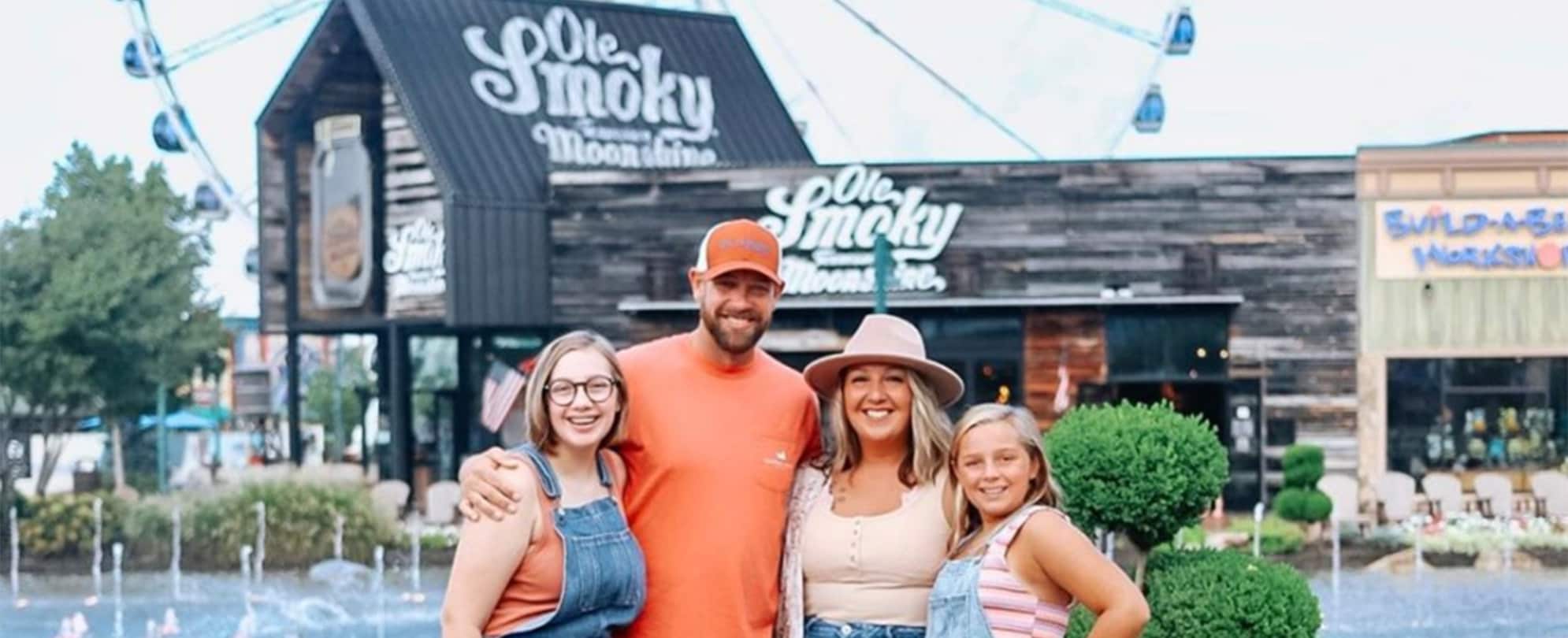 A family of four smiles in front of the Ole Smoky Moonshine Distillery in Gatlinburg, Tennessee