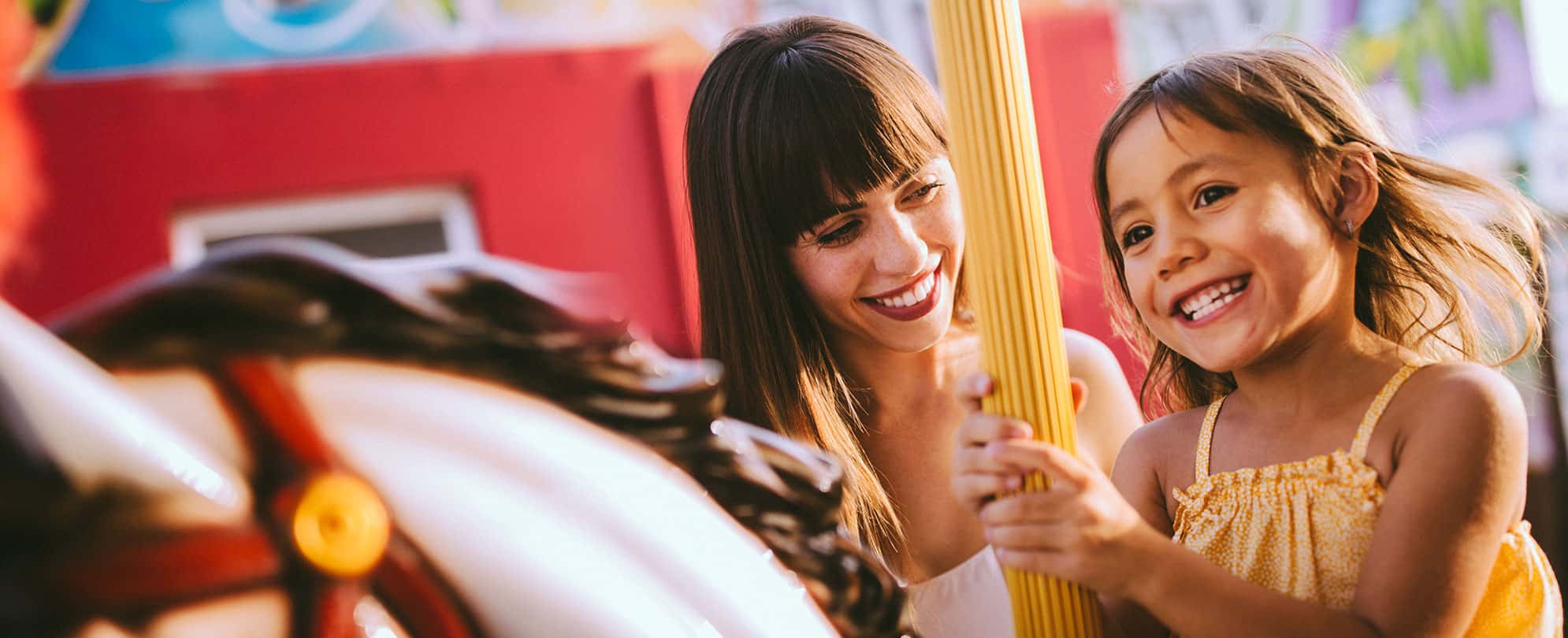 A young girl and her mom smile while riding a merry-go-round in Orlando