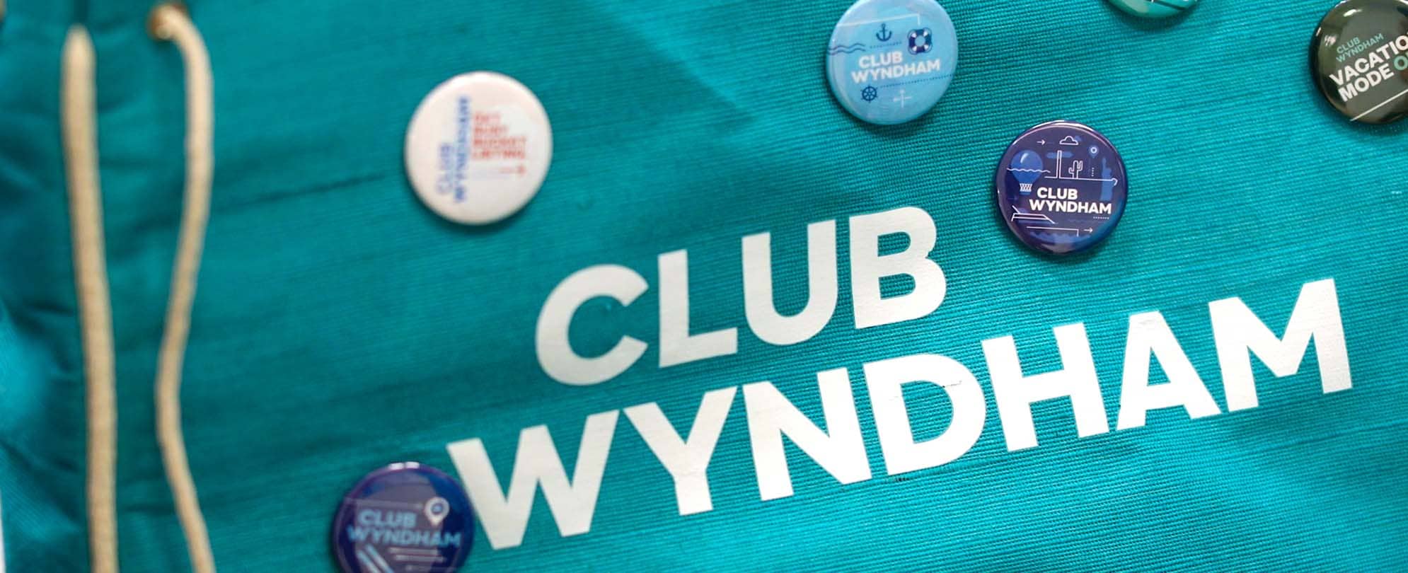 A teal Club Wyndham bag with six Club Wyndham Pinspiration pins on it