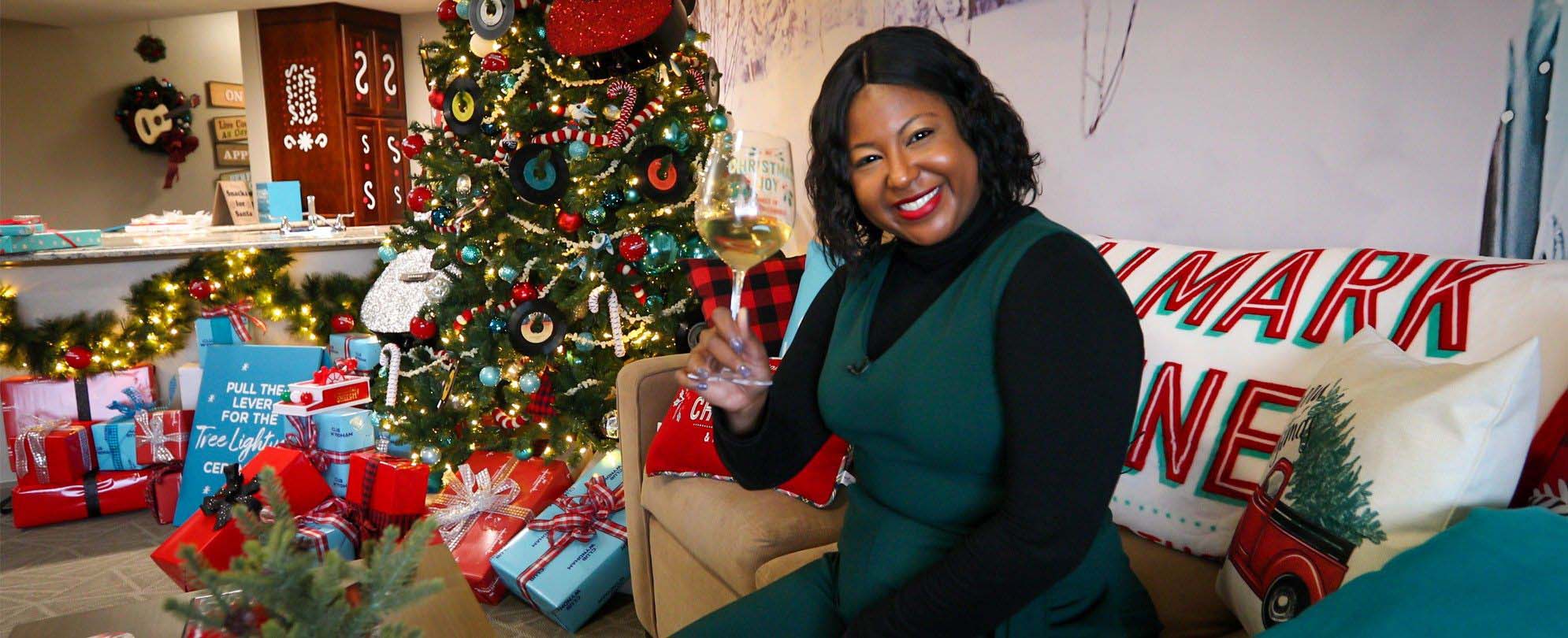 Melody holds up a glass of white wine on the couch in front of a Christmas tree in the Hallmark Channel’s Countdown to Christmas Holiday Suite by Club Wyndham at Club Wyndham Nashville