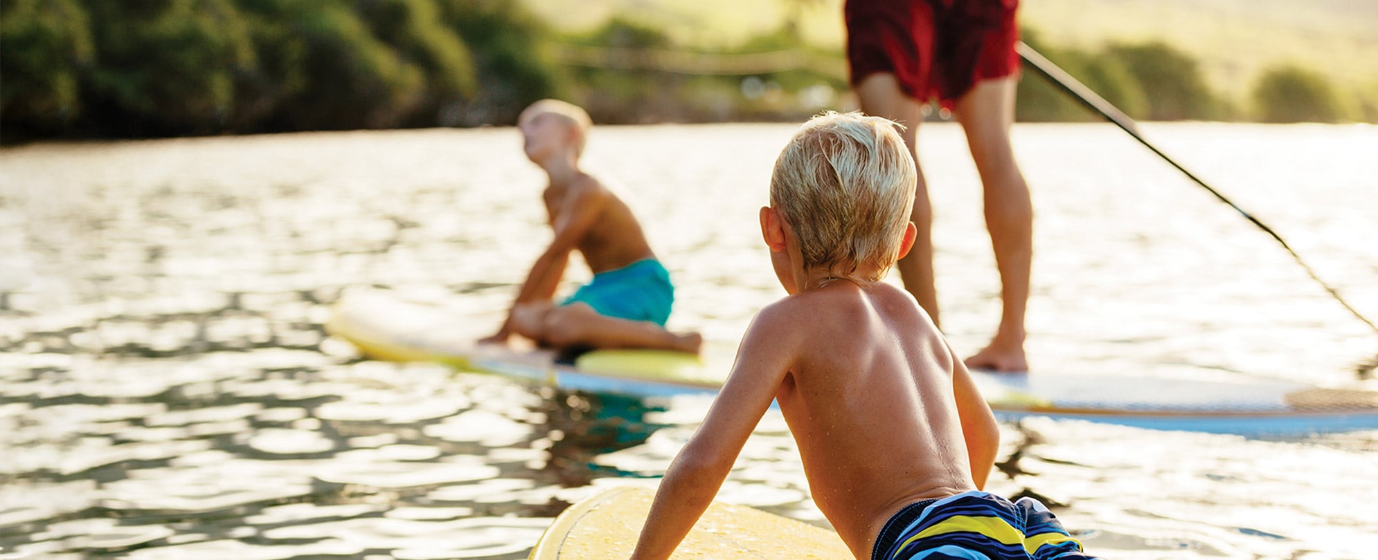 A man and two small boys paddle boarding in the middle of a lake.