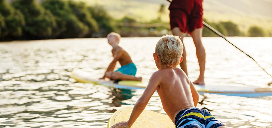 A man and two small boys paddle boarding in the middle of a lake.