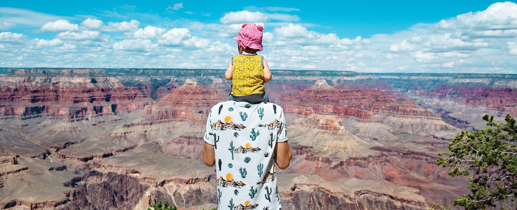 A dad carrying his child on his shoulders as they look out over the Grand Canyon.