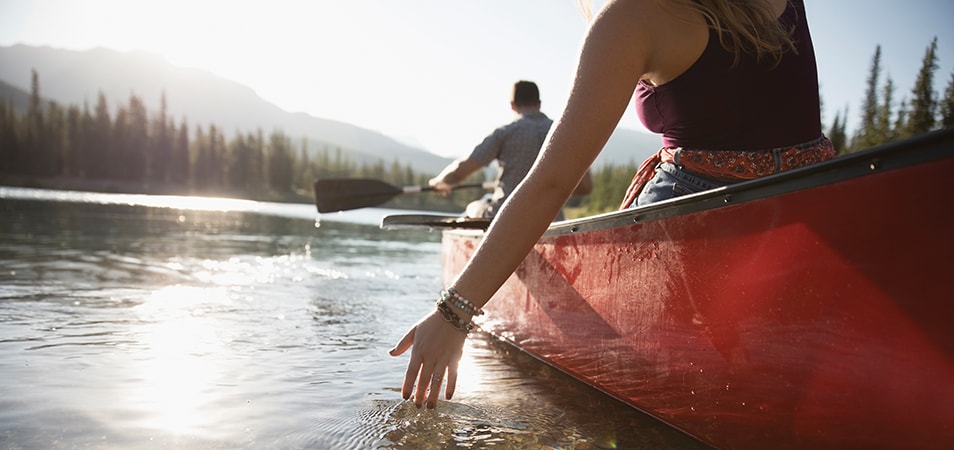 A woman skims her fingertips over the water while kayaking with a friend on a lake