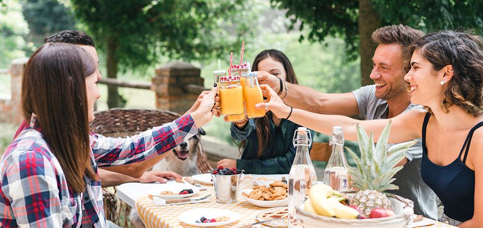 A group of five friends seated at an outdoor table toasting their drinks.