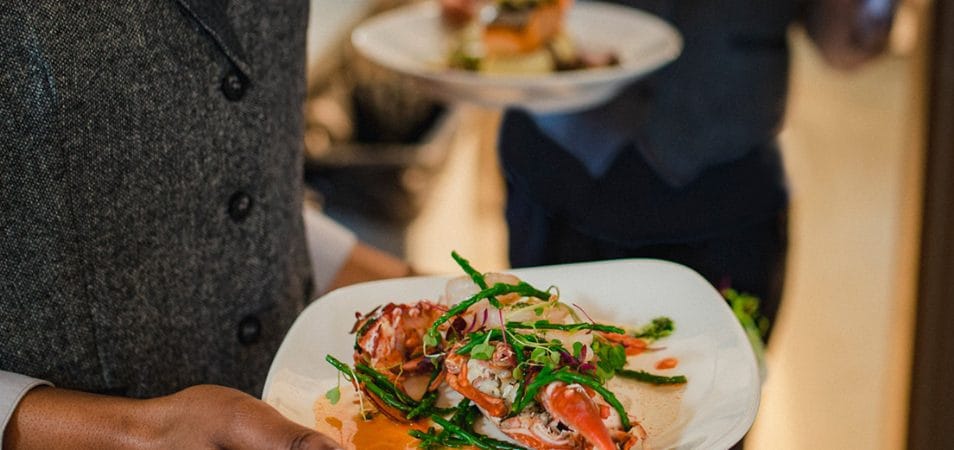 Close-up shot of a waiter holding a plate of seafood and vegetables, about to bring it to a table.